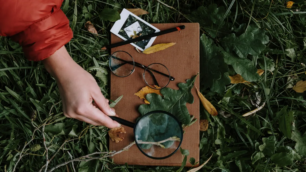 person with magnifying glass outdoors over clipboard